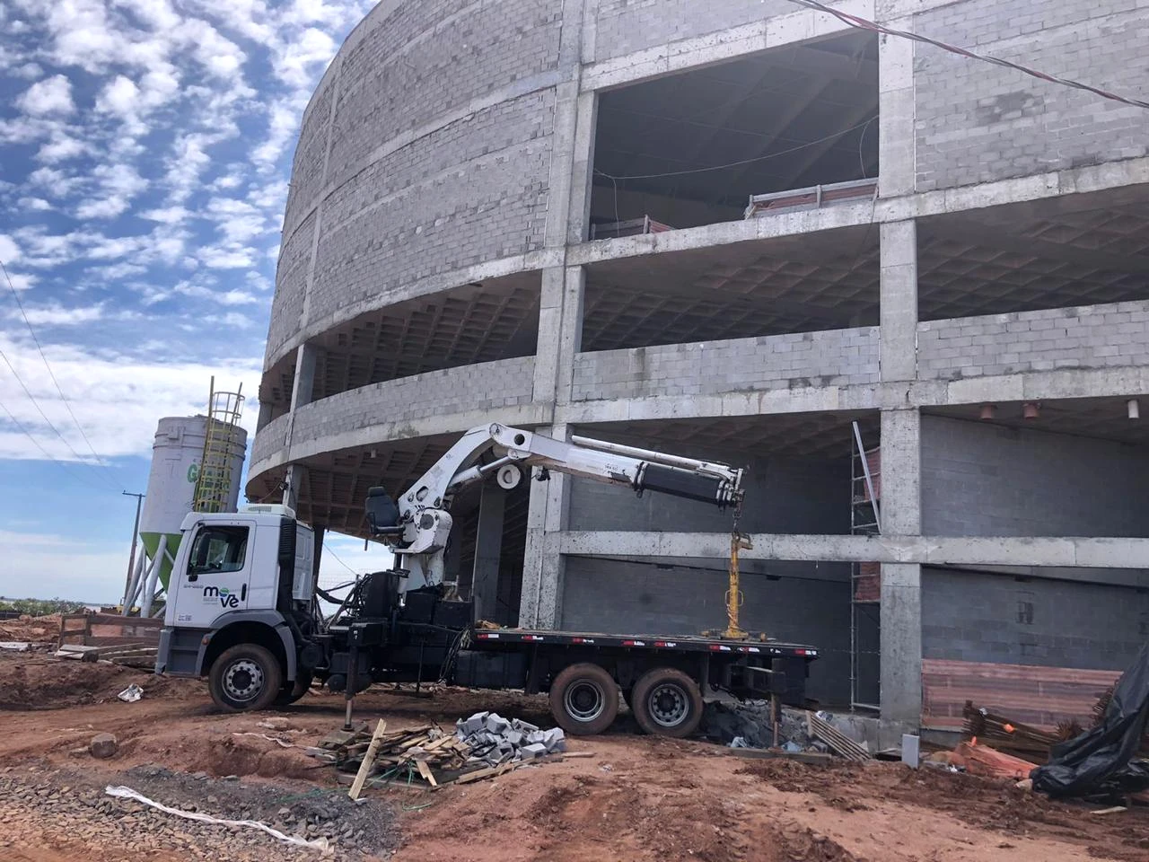 Caminhão munck branco da Move com guindaste estendido ao lado de uma edificação em construção.
