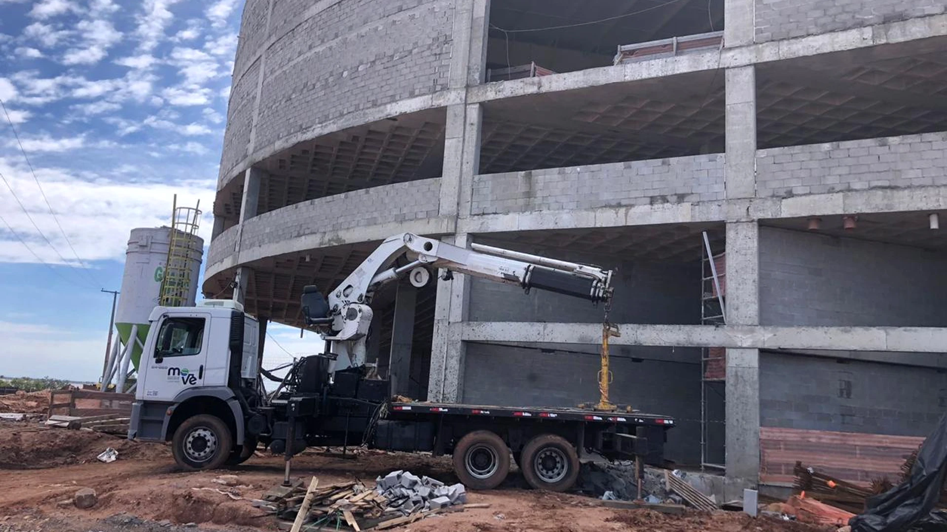 Caminhão munck branco da Move com guindaste estendido ao lado de uma edificação em construção.